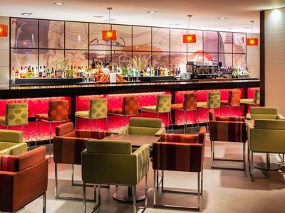 Moderne hotelbar met rode krukken en groene fauteuils rond kleine tafels.