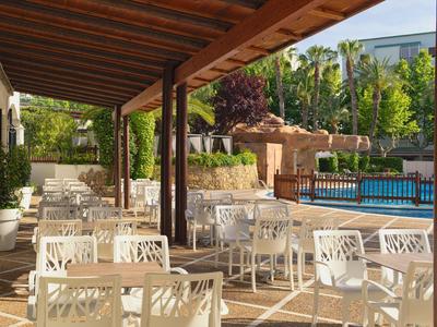 Buitenzitgedeelte bij een zwembad met witte stoelen en tafels onder een houten luifel.