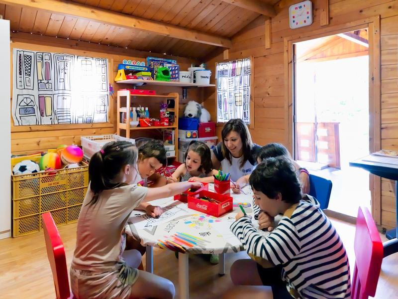 Kinderen en een volwassene spelen samen een bordspel in een knusse houten speelkamer.