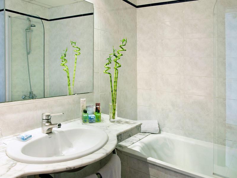 Schone badkamer met witte wastafel, marmeren aanrecht, bad en groene plant.