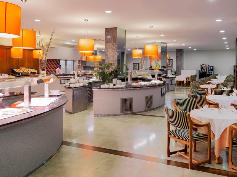 Lichte, moderne hotel eetruimte met ronde buffetstations en netjes gedekte tafels.