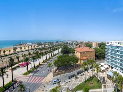 Vue d'une route côtière bordée de palmiers et de bâtiments modernes sous un ciel dégagé.