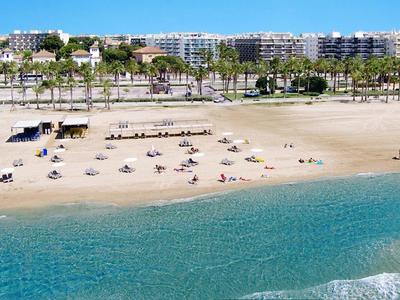 Plage avec chaises longues et plusieurs bâtiments en arrière-plan sous un ciel clair.