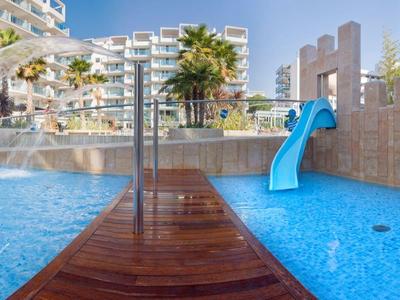 Piscine extérieure moderne avec toboggan aquatique et complexe d'appartements adjacent par temps ensoleillé.