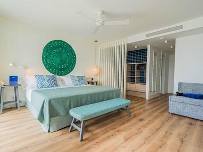 Chambre lumineuse décorée avec un ornement mural vert, grand lit et sol en bois.