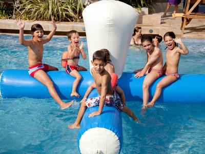 Enfants jouant dans une piscine sur un jouet flottant bleu et blanc, souriants et joyeux.