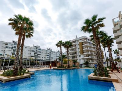 Piscine extérieure entourée de palmiers et bâtiments résidentiels modernes sous ciel nuageux.