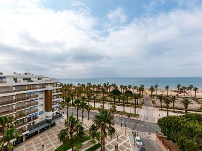 Vue sur la mer depuis un balcon avec palmiers, plage et immeubles modernes.