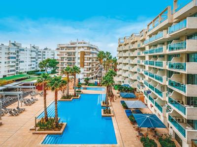 Piscine extérieure moderne au centre d'un complexe hôtelier avec palmiers et balcons.