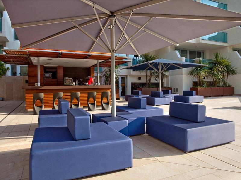 Terrasse d'hôtel avec canapés bleus et grands parasols pour détente en plein air.