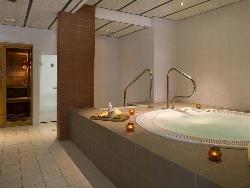 Spa intérieur avec bain à remous, sauna, bougies et serviettes jaunes.