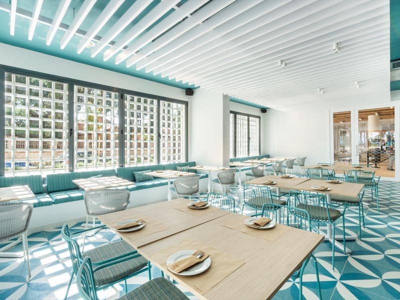 Restaurant lumineux au design moderne, avec des tables en bois angulaires et des banquettes bleues le long des murs.