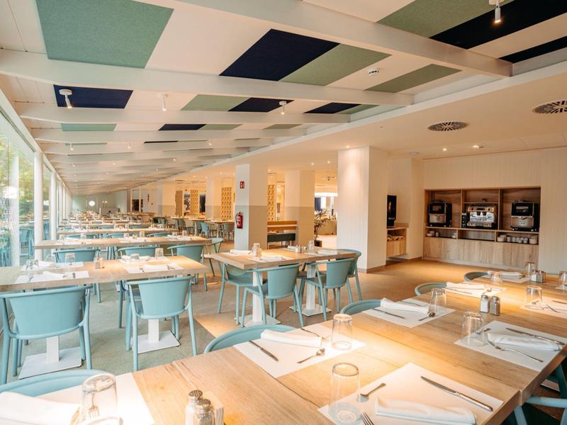 Salle à manger lumineuse et moderne avec tables en bois et chaises bleues dans un hôtel.