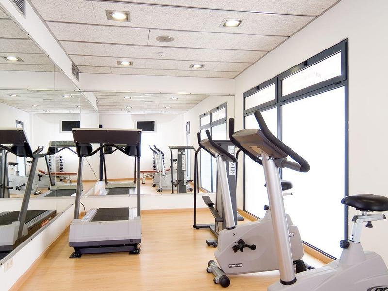 Salle de sport lumineuse avec tapis roulant et vélos d'exercice près de grandes fenêtres.