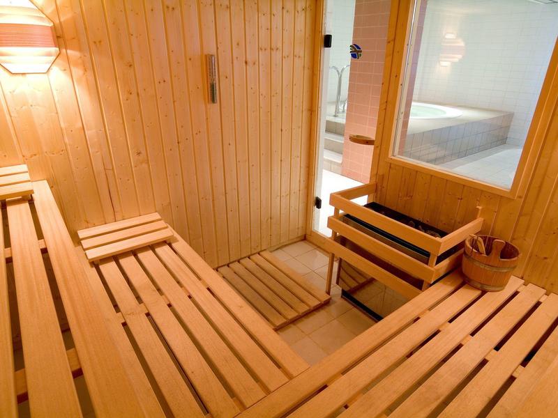 Sauna lumineuse avec bancs en bois, panneaux en bois et poêle de sauna avec seau en bois.