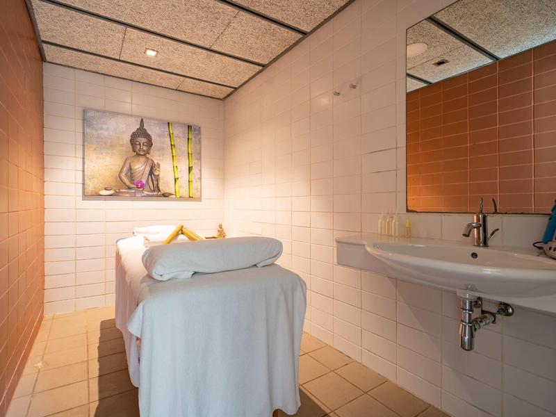 Salle de massage confortable avec table de massage, grand miroir et tableau de Bouddha au mur.