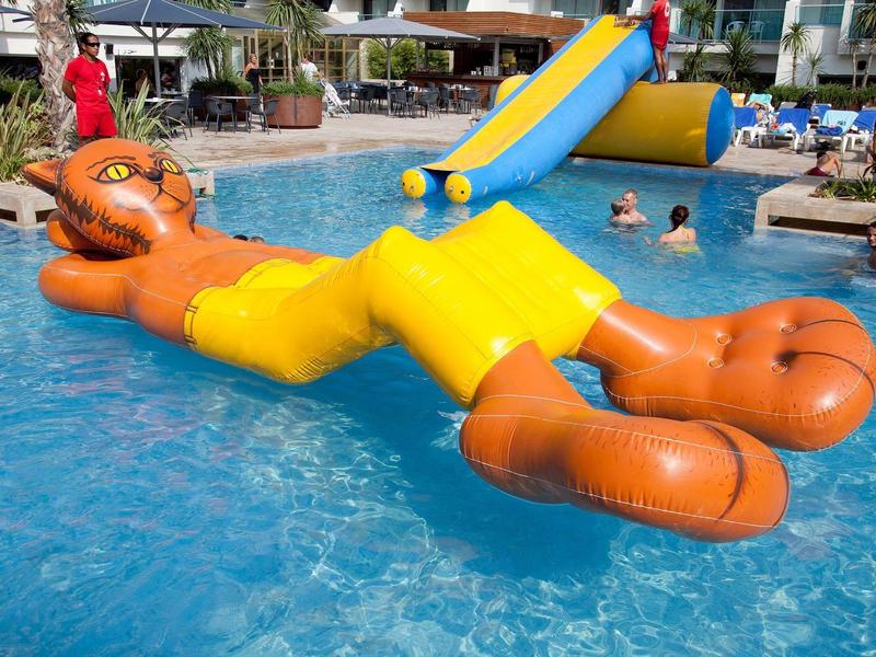 Toboggan gonflable orange et jaune dans une piscine d'hôtel animée.