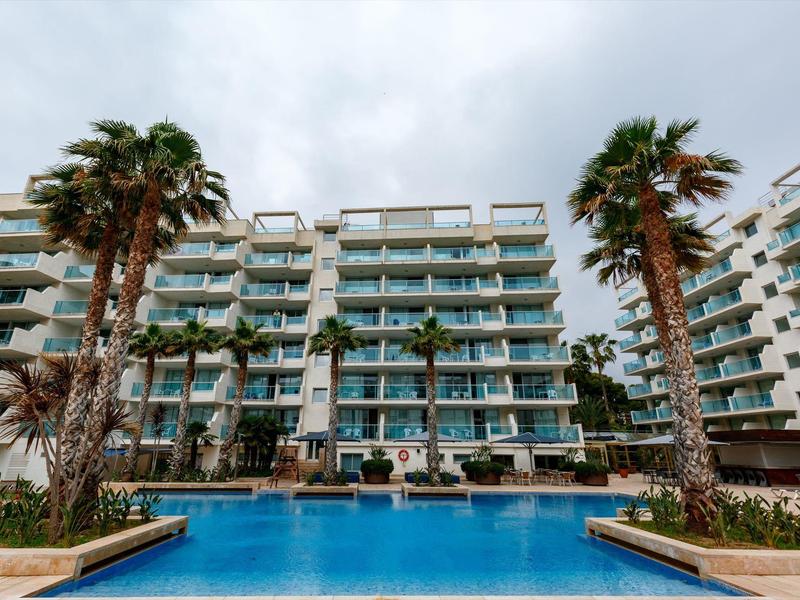 Piscine extérieure avec palmiers devant un hôtel moderne à plusieurs étages.