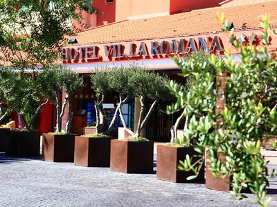 Hotel entrance with modern planters and greenery in front of a coral building.