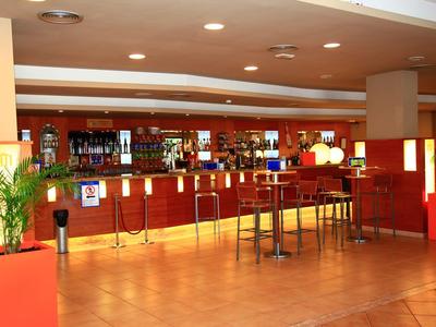 Moderner Hotelbarbereich mit rotem Design, Theke und hohen Tischen.