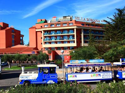 Red hotel with outdoor terrace and tourist train in front on a sunny day.