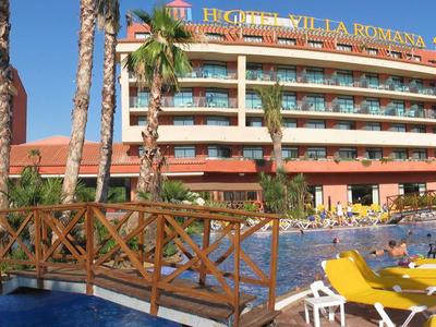 Resort hotel with pool, lounge chairs, palm trees, and wooden bridge under blue sky.