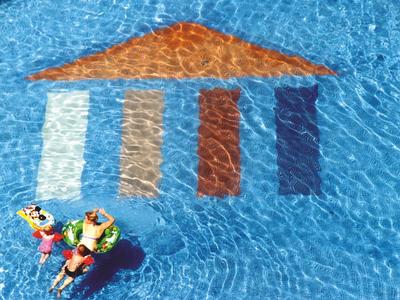 Two people relaxing on pool floats near colorful tiled roof design in clear blue water.