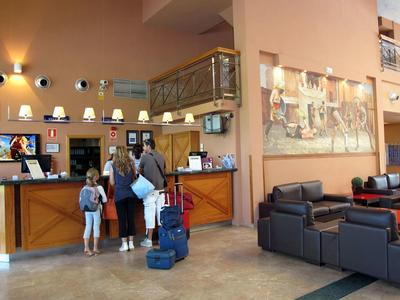 Hotel lobby with guests checking in at reception desk and seating area with sofas.