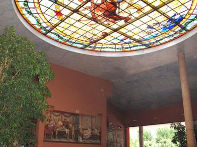 Hotel lobby with stained glass ceiling, plants, seating area, and mosaic floor.