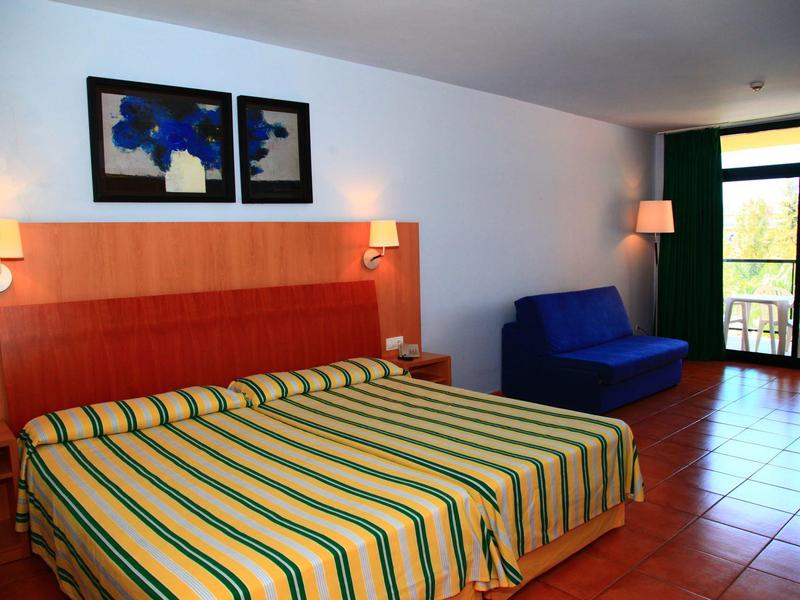 Hotel room with double bed, blue sofa, balcony, and tiled floor.