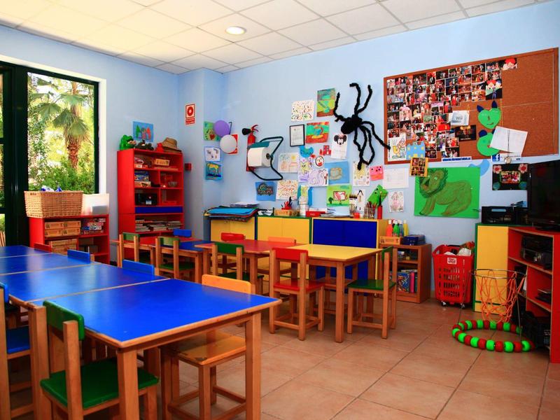 Colorful classroom with blue tables, wooden chairs, and decorated bulletin boards.