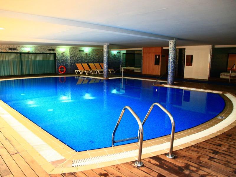 Indoor swimming pool with blue water, wooden deck, and lounge chairs in the background.