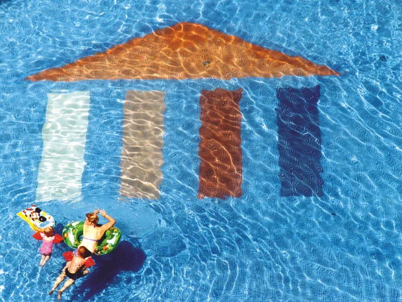 Two people relaxing on pool floats near colorful tiled roof design in clear blue water.