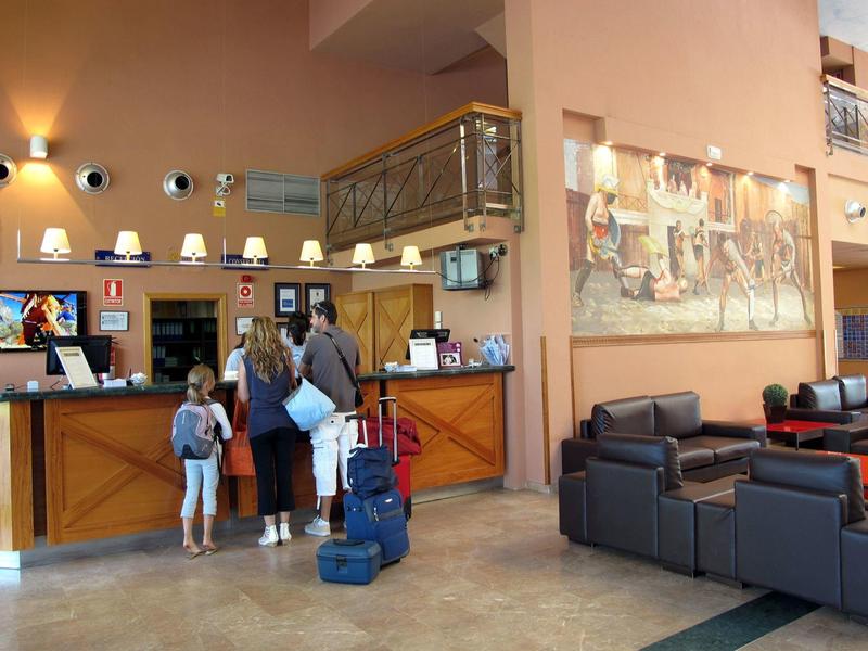 Hotel lobby with guests checking in at reception desk and seating area with sofas.
