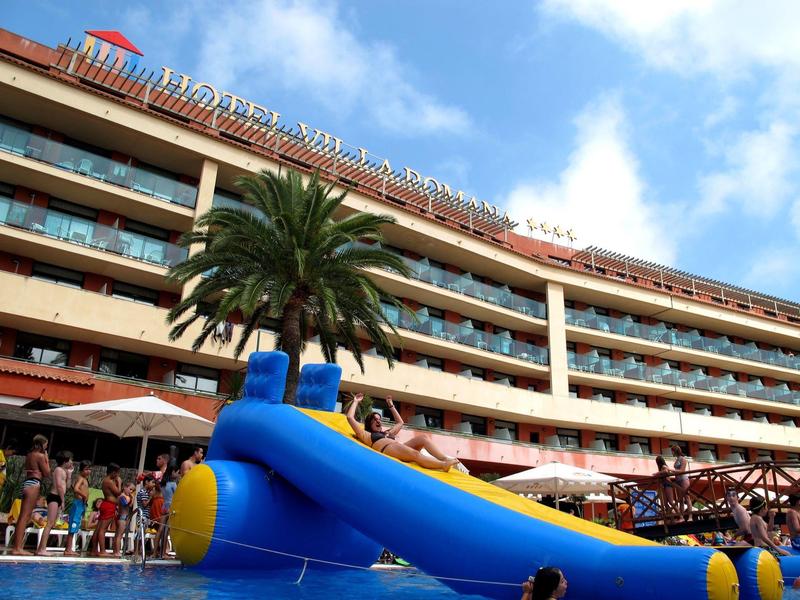 Outdoor pool area with inflatable slide and hotel building under blue sky.