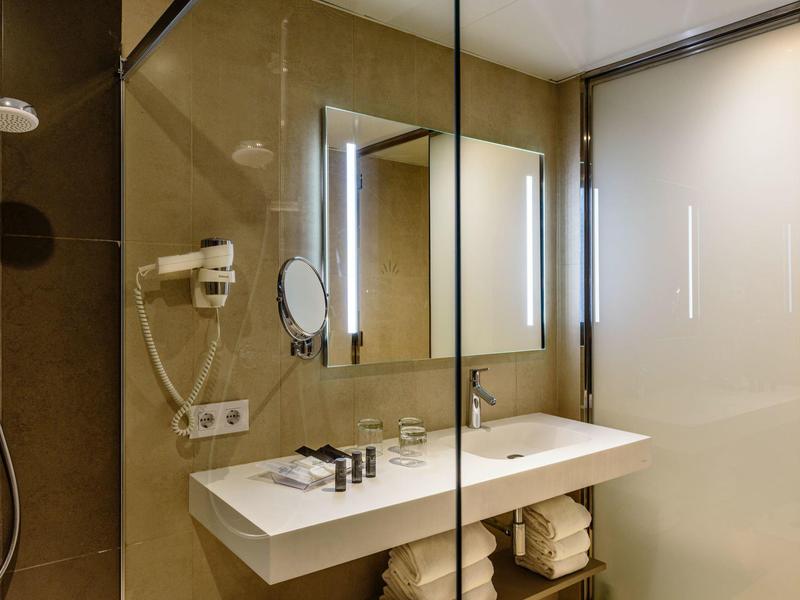 Baño moderno con lavabo doble, espejo iluminado y mampara de cristal.