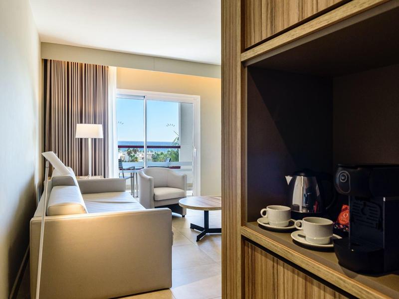 Habitación de hotel moderna con sofá, sillones, ventana grande y máquina de café en un estante de madera.