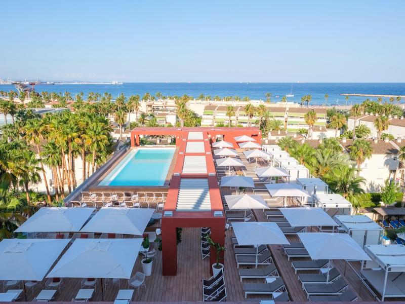 Piscina moderna del hotel con tumbonas y vista al mar azul bajo cielo despejado.