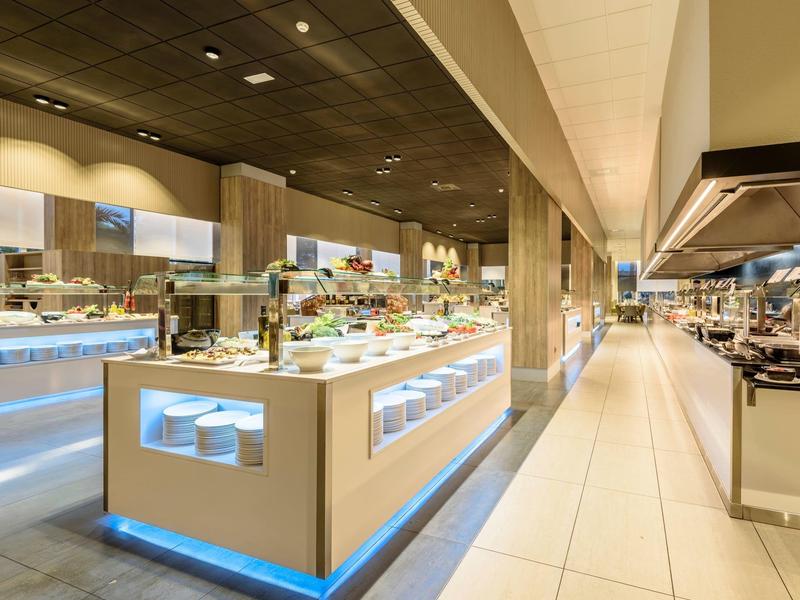 Área de buffet moderno en hotel con islas de comida iluminadas y diseño espacioso.