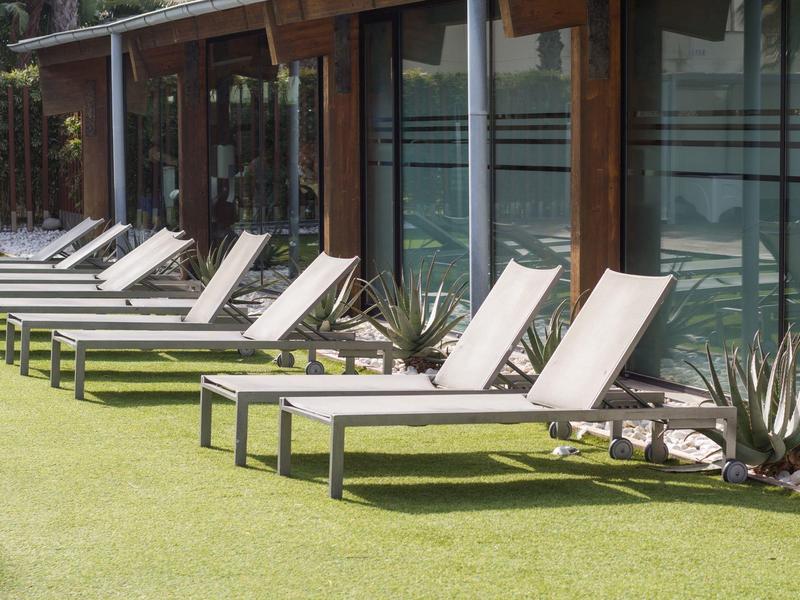 Varias tumbonas blancas con patas negras sobre césped verde junto a un edificio con grandes ventanas.