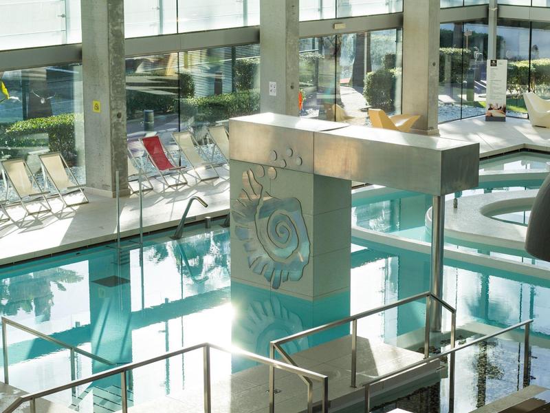 Lobby de hotel moderno con paredes de vidrio, suelo brillante y sofás junto a la piscina.