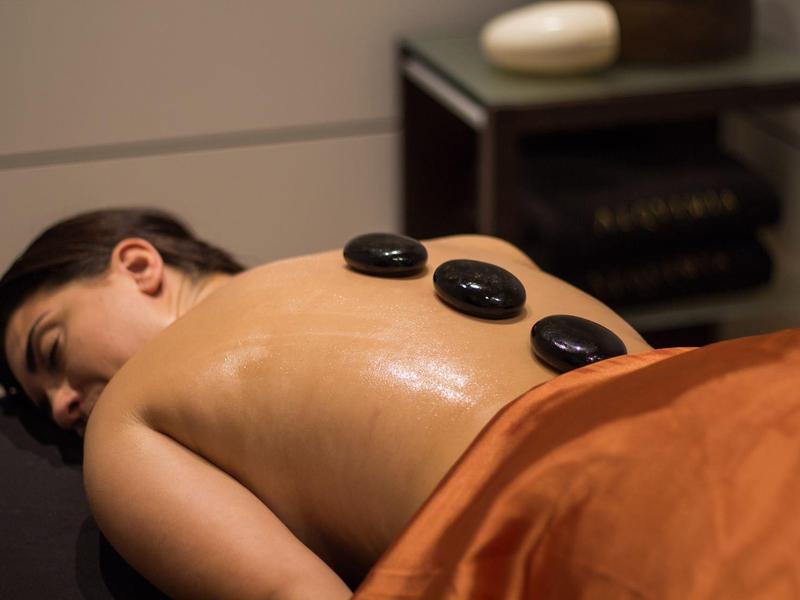 Mujer relajada con piedras calientes sobre la espalda en un área de bienestar.