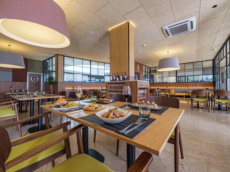 Restaurante de hotel moderno con mesas puestas, sillas y grandes ventanas para luz natural.