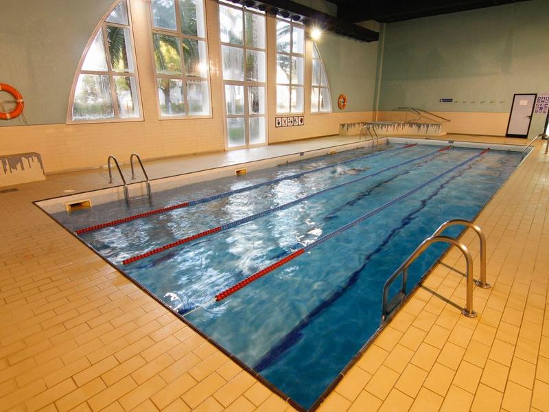 Habitación de hotel moderna con cama doble, sofá, escritorio y grandes ventanas que permiten luz natural.