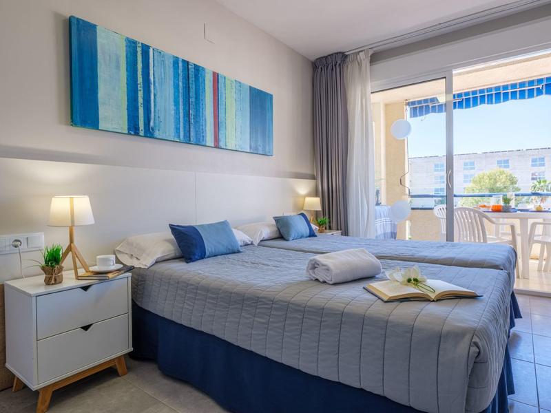 Habitación de hotel moderna con cama doble, tonos azules y balcón con vista al mar.