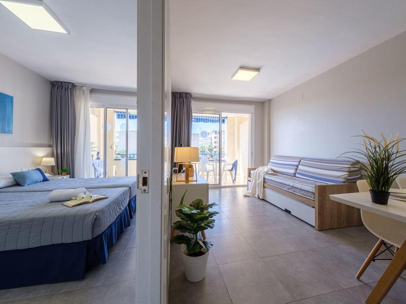 Habitación de hotel moderna con cama doble, sofá, escritorio y grandes ventanas que permiten luz natural.