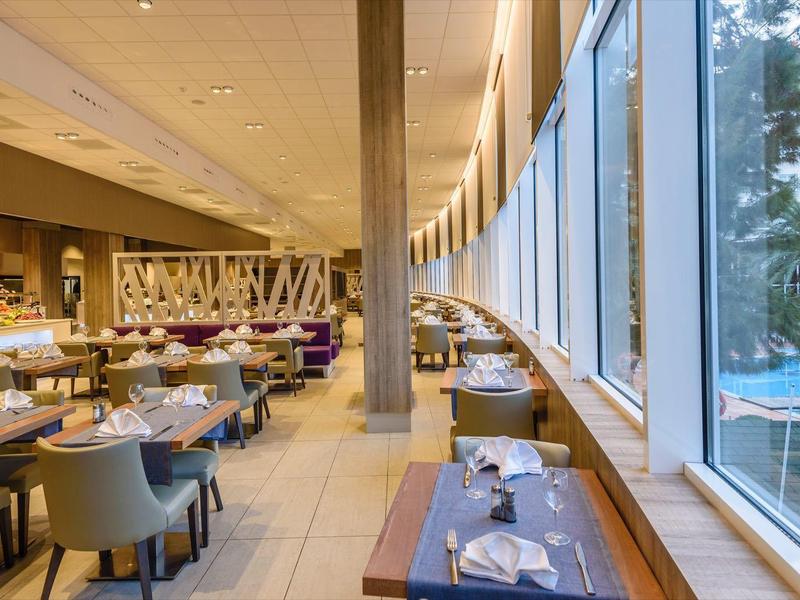 Restaurante moderno con grandes ventanales, vista a la piscina y mesas elegantes.