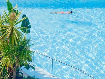 Una persona nuota in una piscina blu chiaro accanto a piante tropicali verdi.