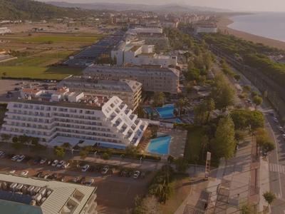 Vista aerea di un hotel costiero con più edifici, una piscina e una strada adiacente.