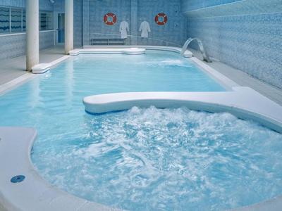 Binnenzwembad met whirlpool gedeelte in een lichte wellnessruimte met blauwe tegels